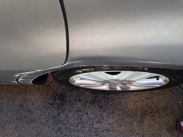 A minor scrape on a Honda Jazz, rear wheel arch. This damage includes the door and has pushed the outer skin and inner arch in, and also needs paint - a proper repair would be expensive, but the car's usability is unchanged.