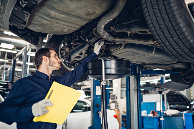 MoT tester under a car on a ramp checking components as part of the MoT test